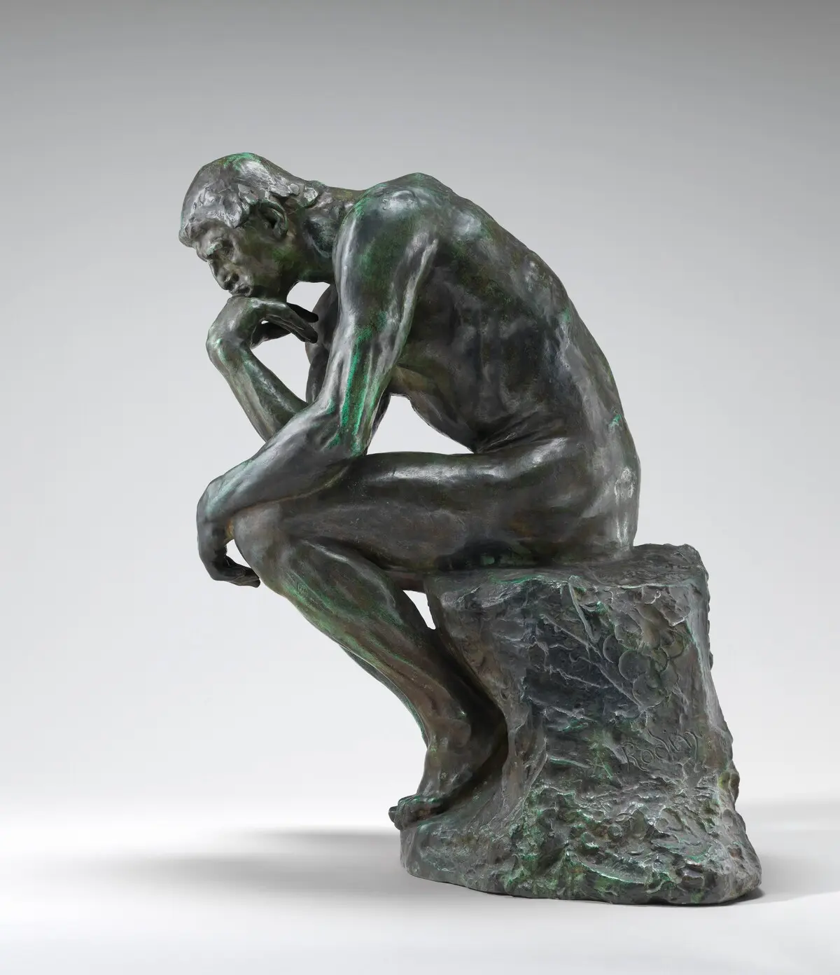 Bronze sculpture of a seated male figure leaning forward in concentrated thought.
